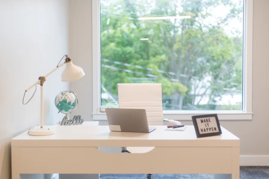 A bright home office desk with a laptop, lamp and a window looking onto trees