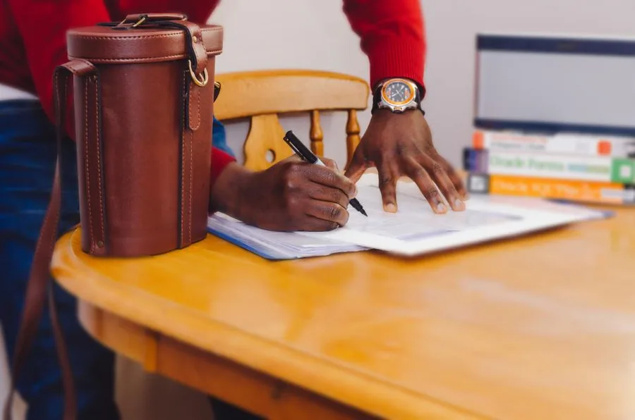 Hands writing notes in a workbook on a warm wooden table